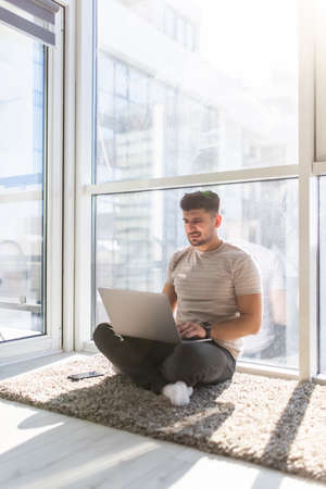 Young man working on laptop sitting on floor. Guy with computer reading news, surfing net or...