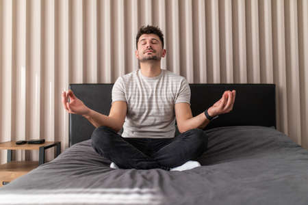 Young man meditating in bedroomの写真素材