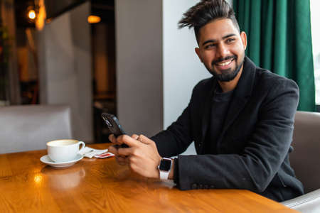 Young indian man using phone white sitting in cafe