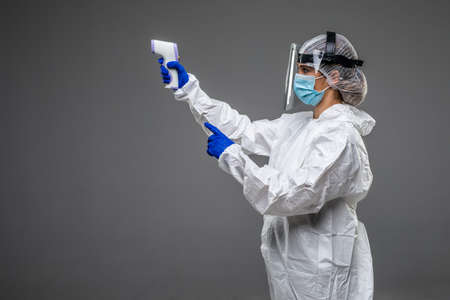 male doctor wearing protective clothing, glasses, mask and gloves, with a non-contact thermometer to measure temperature, on a white background, coronavirus epidemic conceptの写真素材