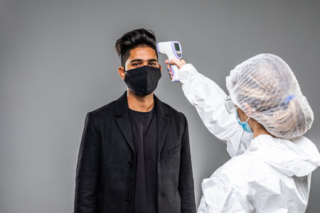 Doctor measures the temperature of a man in a medical mask. Novel Wuhan coronavirus 2019-nCoV epidemic outbreak. Medical Digital Non-Contact Infrared Thermometer, covid-19 checkpointの写真素材