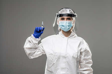 Biological hazard. An asian woman in a protective suit and mask holds an injection syringe and vaccine.の写真素材