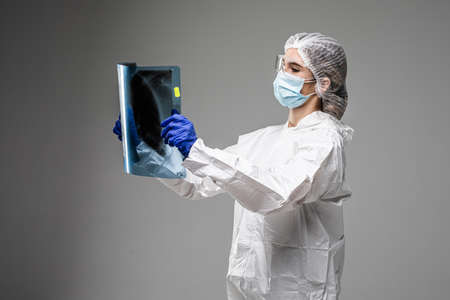Female pulmonologist or oncologist holding chest X-ray scan, inspecting  patient lungs, wearing PPE uniformãの写真素材