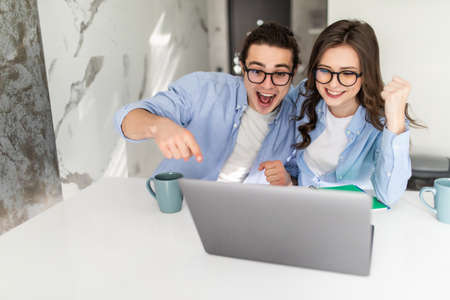 Excited young couple celebrating success, reading good news in email, looking at laptop screen,...