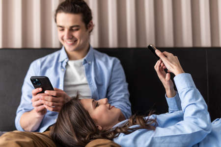 Young couple using wireless technology sitting with their phones lying in the bed