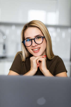 Shot of pretty young woman working with laptop and documents in the kitchen at home.の写真素材
