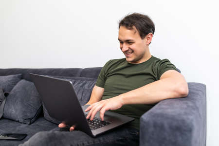Happy smiling young man watching and working on computer laptop at homeの写真素材