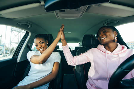 Two african woman inside the car driving and give five on the cityの写真素材