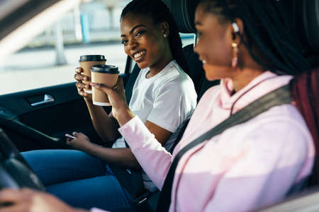 Two african woman drinkink coffee in the car while driving car on the travelの写真素材