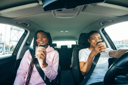 Happy friends with cup of coffee in car. Holiday trip of friendsの写真素材