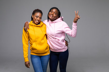 Portrait of a two african girlfriends showing two fingers sign on gray background and looking at cameraの写真素材