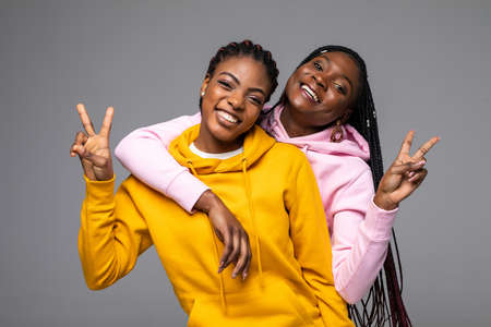 Photo of two pretty african women make peace gesture.standing isolated over gray background.の写真素材