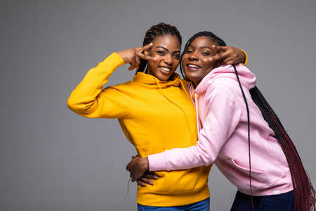 Portrait of a two african girlfriends showing two fingers sign on gray backgroundの写真素材