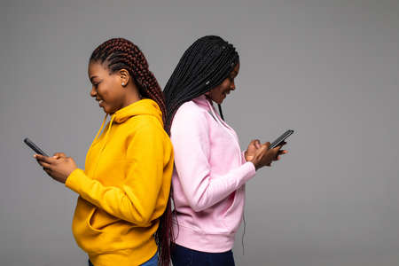 Two african women using cell phones isolated over gray backgroundの写真素材