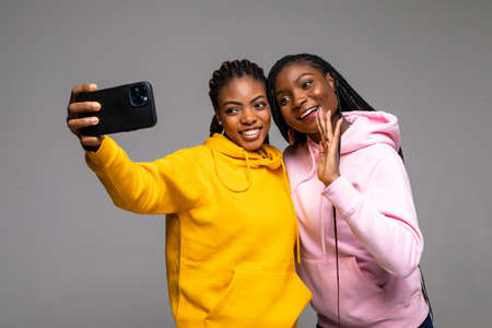 Portrait of two african young womens taking selfie on smartphone isolated over gray backgroundの写真素材