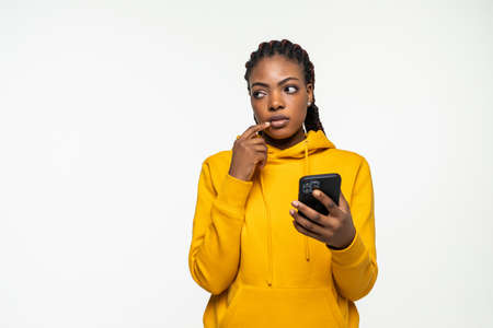 Shocked young african american woman using mobile cell phone typing sms message on white background. People lifestyle concept.の写真素材