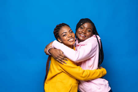Portrait of two african women hugging and laughing on the blue backgroundの写真素材