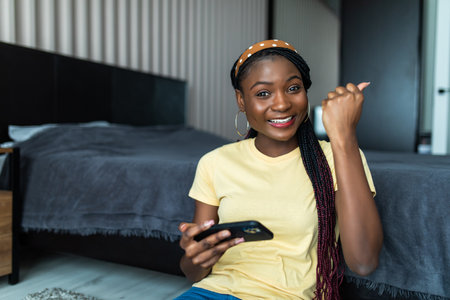 Happy african american young woman lying on floor with phone and headphones listening to music at...