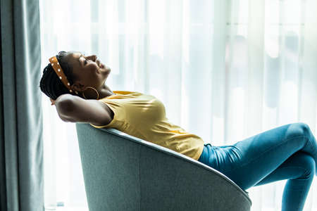 Smiling African American woman resting in rocking chair close up, satisfied girl resting in cozy chair at home, spending lazy day weekend, daydreamingの写真素材