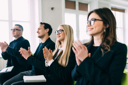 Group of happy business people in smart casual wear sitting together at the table and applauding to someoneの写真素材
