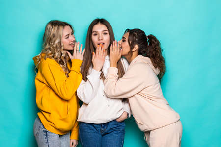 Three attractive girls gossiping isolated over turquoise background
