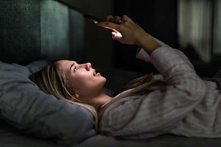 Insomnia. Young woman using mobile phone in the dark in her bed