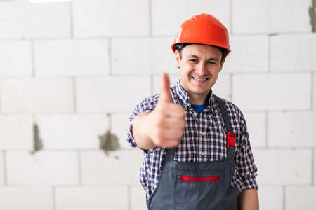 Portrait of male making approving gesture near concrete wall. Prudent builder in protective outfit...