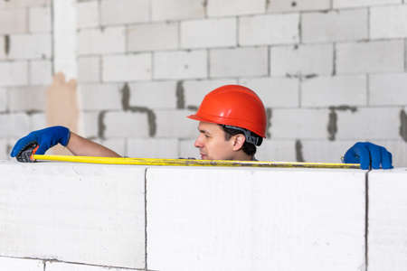 The bricklayer measures a newly built wall with a tape measure. Construction