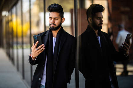 Handsome hipster modern businessman with beard walking in town with mobile phone