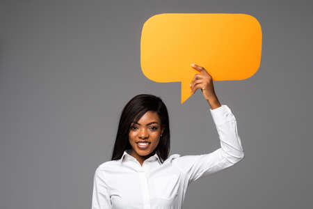 Portrait of young african business woman holding empty speech bubble isolated over gray backgroundの写真素材