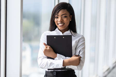 African businesswoman talking on mobile phone and holding clipboard in office