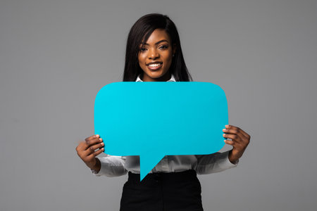 Portrait of young african business woman holding empty speech bubble isolated over gray background
