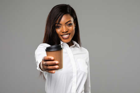 african american businesswoman with business newspaper and coffee to go isolated on gray background