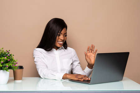 Young African businesswoman sitting at the desk in the office and video-calling chatting with...