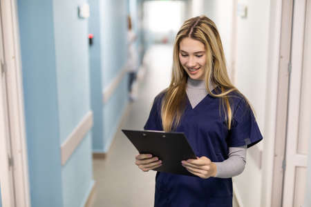 Portrait of female nurse working in hospital. Woman healthcare worker with clipboard in corridor.