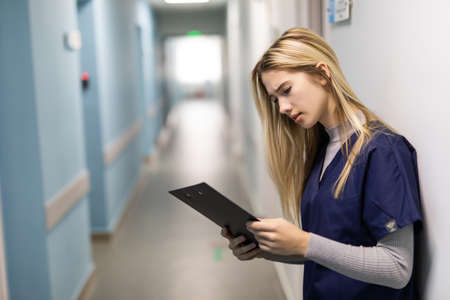 female doctor in hospital corridor holding clipboard and smiling to you