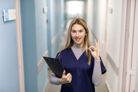 Cheerful beautiful young woman doctor with clipboard showing ok signの写真素材