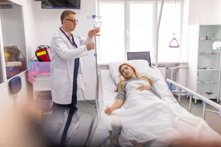 Doctor connects the dropper. Patient lying bed of hospital while get treatment.の写真素材