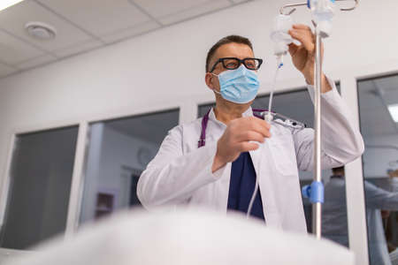 Doctor take care or look after patient by himself. Doctor checking Intravenous drip, IV tube saline fluid bag for cure patient in hospital room. He concern his sick person so much. health careの写真素材