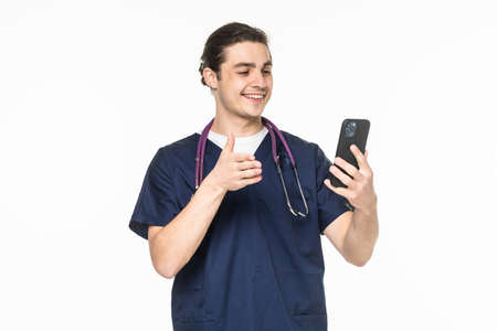 Medicine, healthcare and technology concept. Happy smiling doctor or male nurse in blue uniform with stethoscope having video call on phone over white backgroundの写真素材
