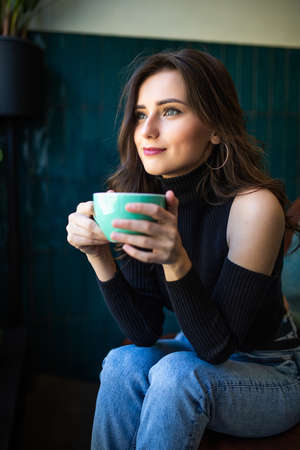 Young pretty woman in a good mood with cup of coffee sitting in cafe.の写真素材