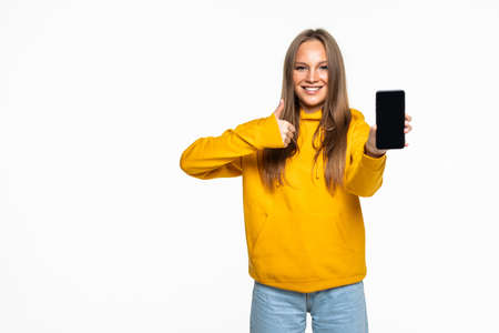 Happy young woman holding blank screen mobile phone and pointing finger over white backgroundの写真素材