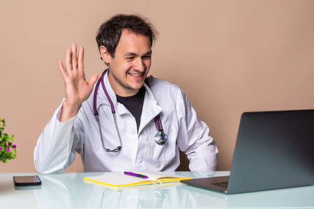 Doctor online. Male doctor works talking video call with patient using bast shoe while sitting at desk in back view clinic office.の写真素材
