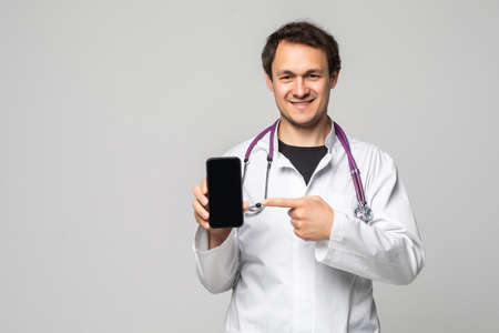 Shot of man doctor isolated on white background, presenting smart phone and pointing with finger at blank black screen with copyspace for adsの写真素材