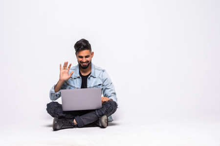 Young man sitting on the floor make video call with a laptop on white backgroundの写真素材