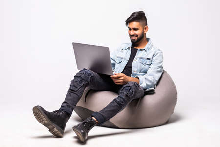 Handsome man working on a laptop and sitting on a floor, isolated against white backgroundの写真素材