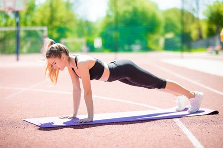 Slim beautiful athletic woman doing planking exercise in the stadiumの写真素材