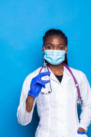 healthcare, vaccination, anesthesia and medical concept - african american female doctor holding syringe with injection over blue backgroundの写真素材