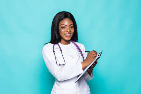happy african medical intern doctor writing on clipboard isolated on turquoise background