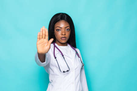 Young afro american doctor woman over isolated background doing stop sing with palm of the hand. Warning expression with negative and serious gesture on the face.の写真素材